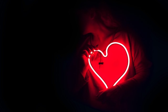 Girl holding light in the shape of heart in dark