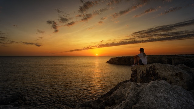 Person sitting on rock watching sunset