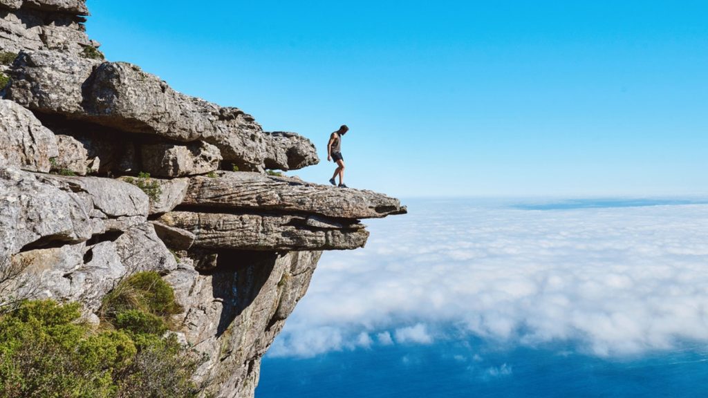 Man standing at edge of cliff with blue sky